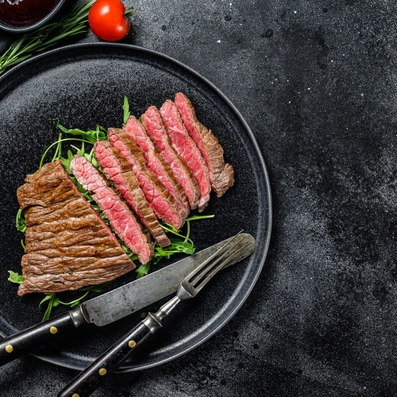 Flat Iron Steak on a Black plate with cutlery