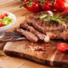 Cooked Rump Steak served on a wooden board with a side salad