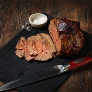 Cooked and sliced topside of beef joint on a piece of slate with salt surrounding.