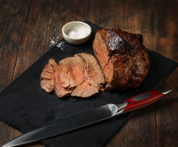 Cooked and sliced topside of beef joint on a piece of slate with salt surrounding.