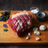 Raw, topside of beef joint on a plank of wood with garlic and salt surrounding.