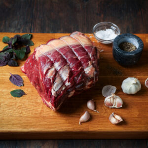 Raw, topside of beef joint on a plank of wood with garlic and salt surrounding.