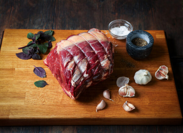 Raw, topside of beef joint on a plank of wood with garlic and salt surrounding.