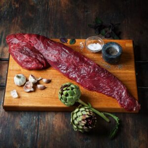 Whole beef fillet displayed on a wooden board with fresh artichoke.