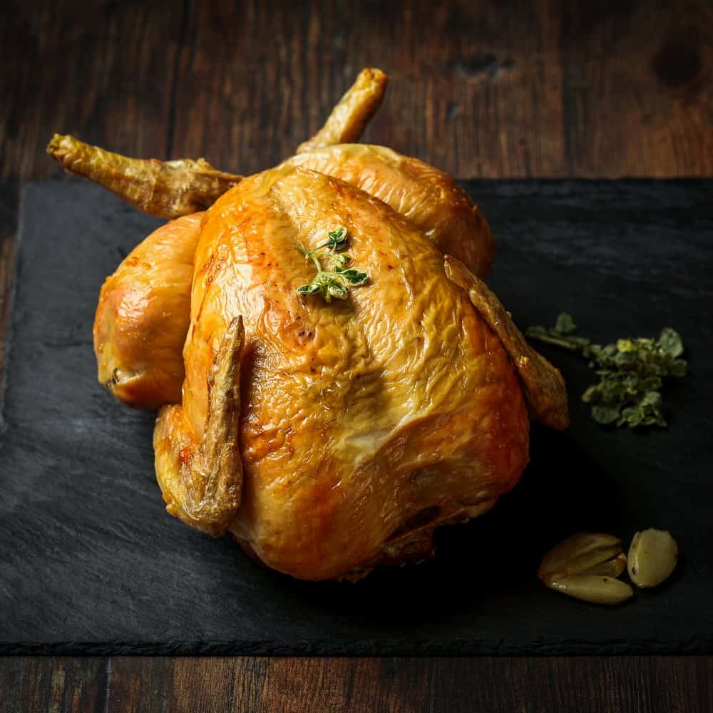 Golden, crispy fried whole chicken placed on a black stone board